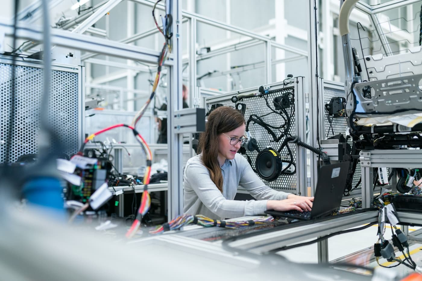 An engineer working at a laptop on a manufacturing floor, surrounded by production equipment.